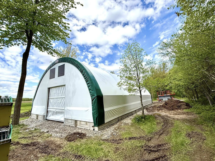 Bâtiment en toile avec charpente d’acier galvanisé installé en bordure de forêt